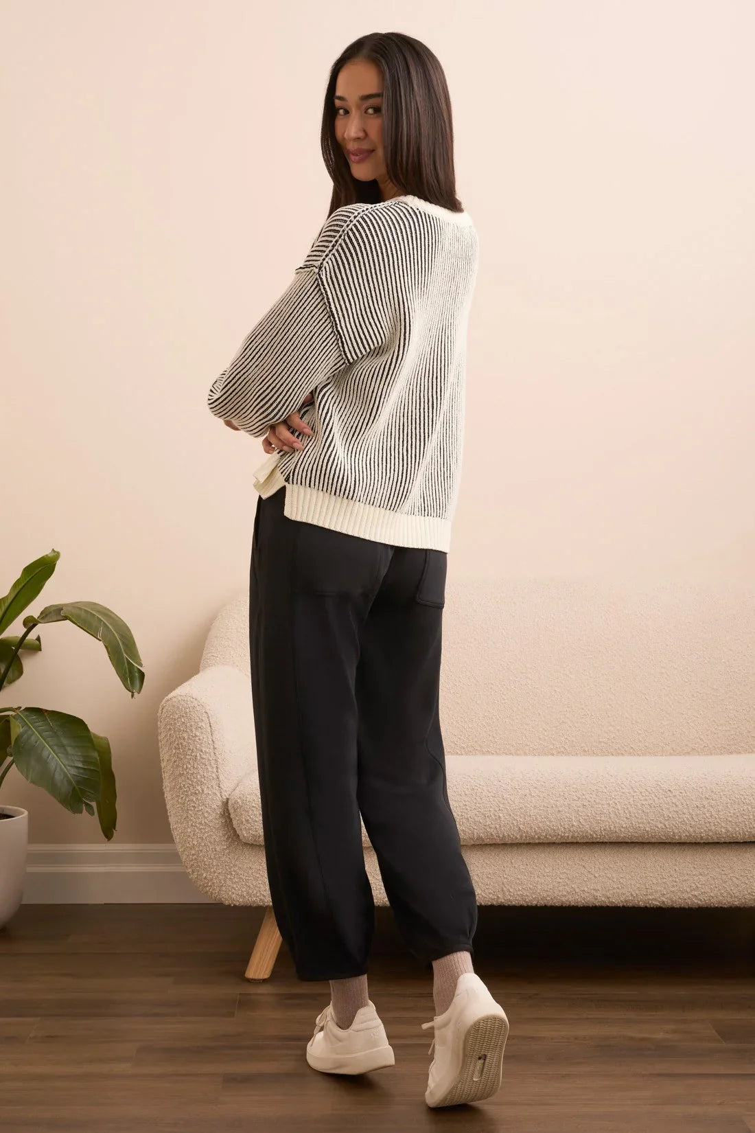 Woman modeling a black and white striped sweater with relaxed black pants, standing in a modern living room
