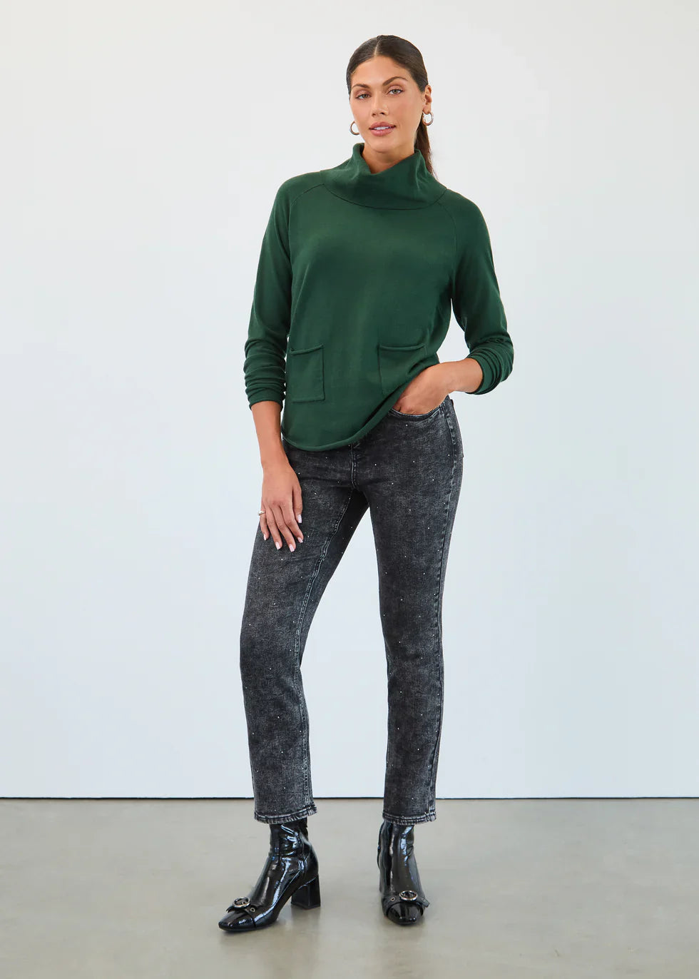 Woman modeling an evergreen mock neck pullover and black speckled jeans