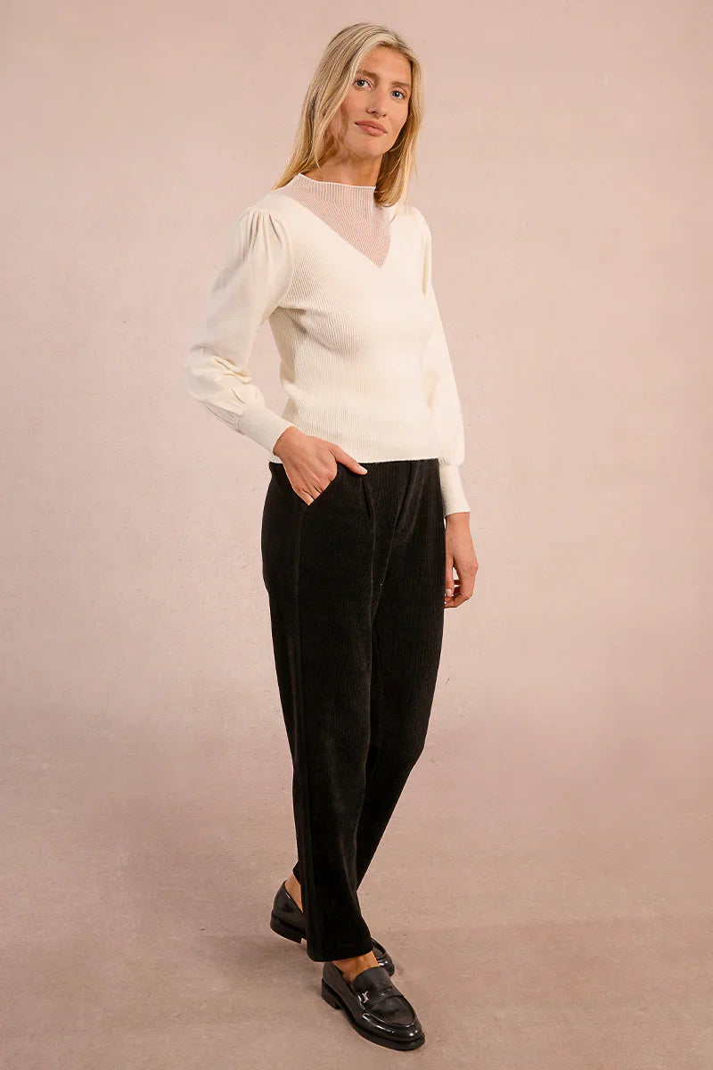 Woman modeling ivory knit top with sheer yoke and black pants
