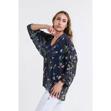 Model wearing a navy blue floral sheer blouse with relaxed fit and white pants