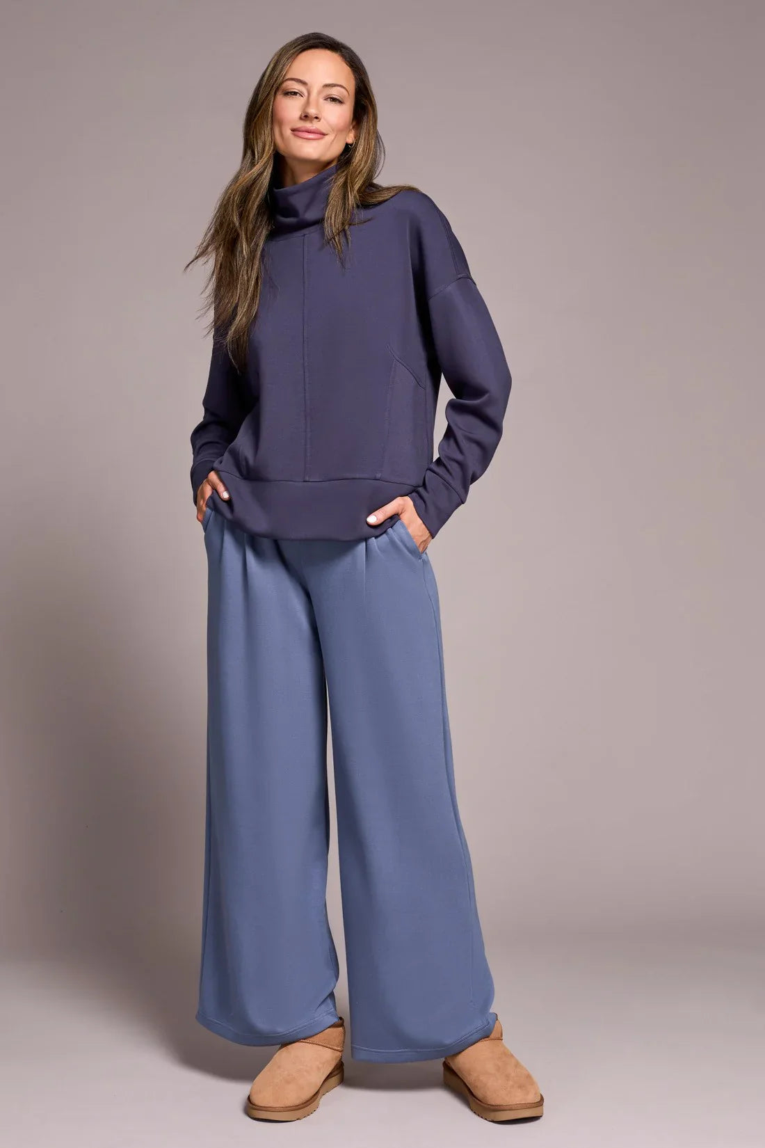 Woman modeling a cozy navy turtleneck loungewear set with light blue wide-leg pants and tan slippers