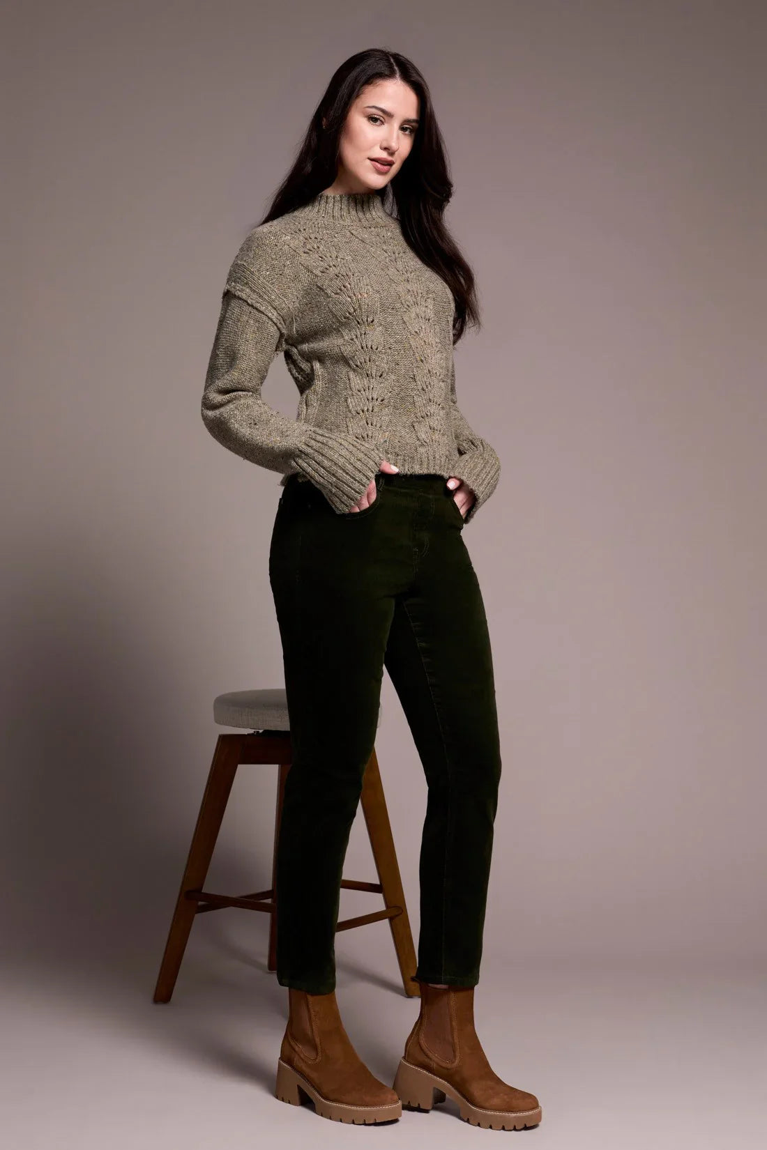 Woman in olive corduroy pants and taupe sweater, standing by a stool