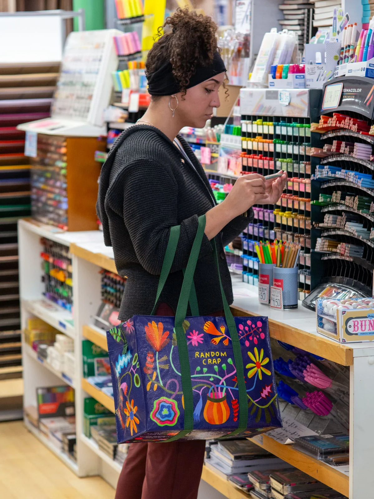 Woman shopping for stationery, carrying a vibrant floral reusable tote bag labeled 'Random Crap'