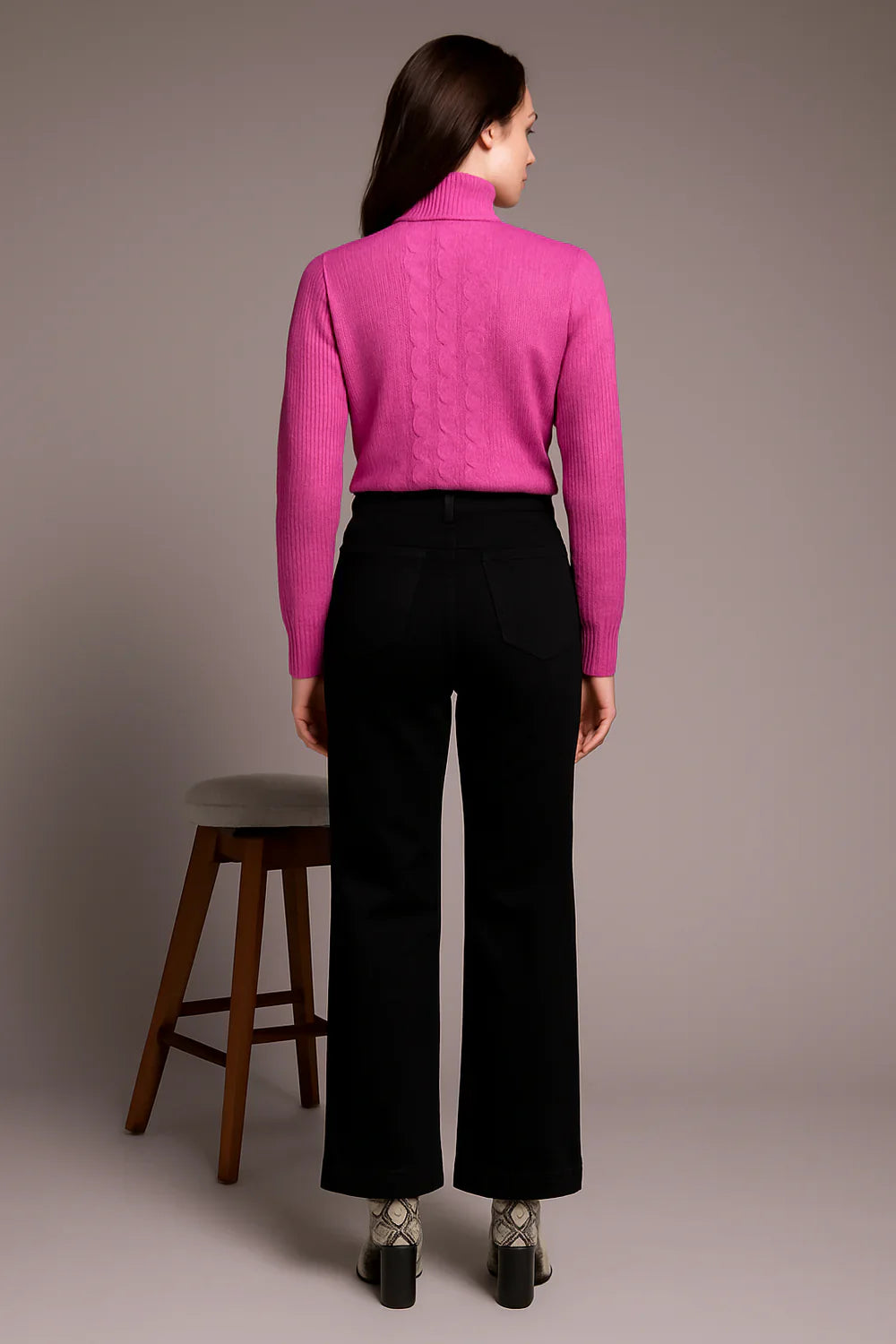 Back view of a woman wearing a vibrant pink cable knit turtleneck sweater with black pants