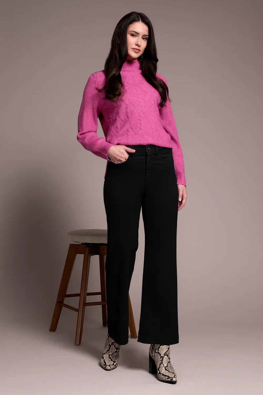 Front view of a woman in a bold pink cable knit turtleneck sweater paired with black wide-leg pants