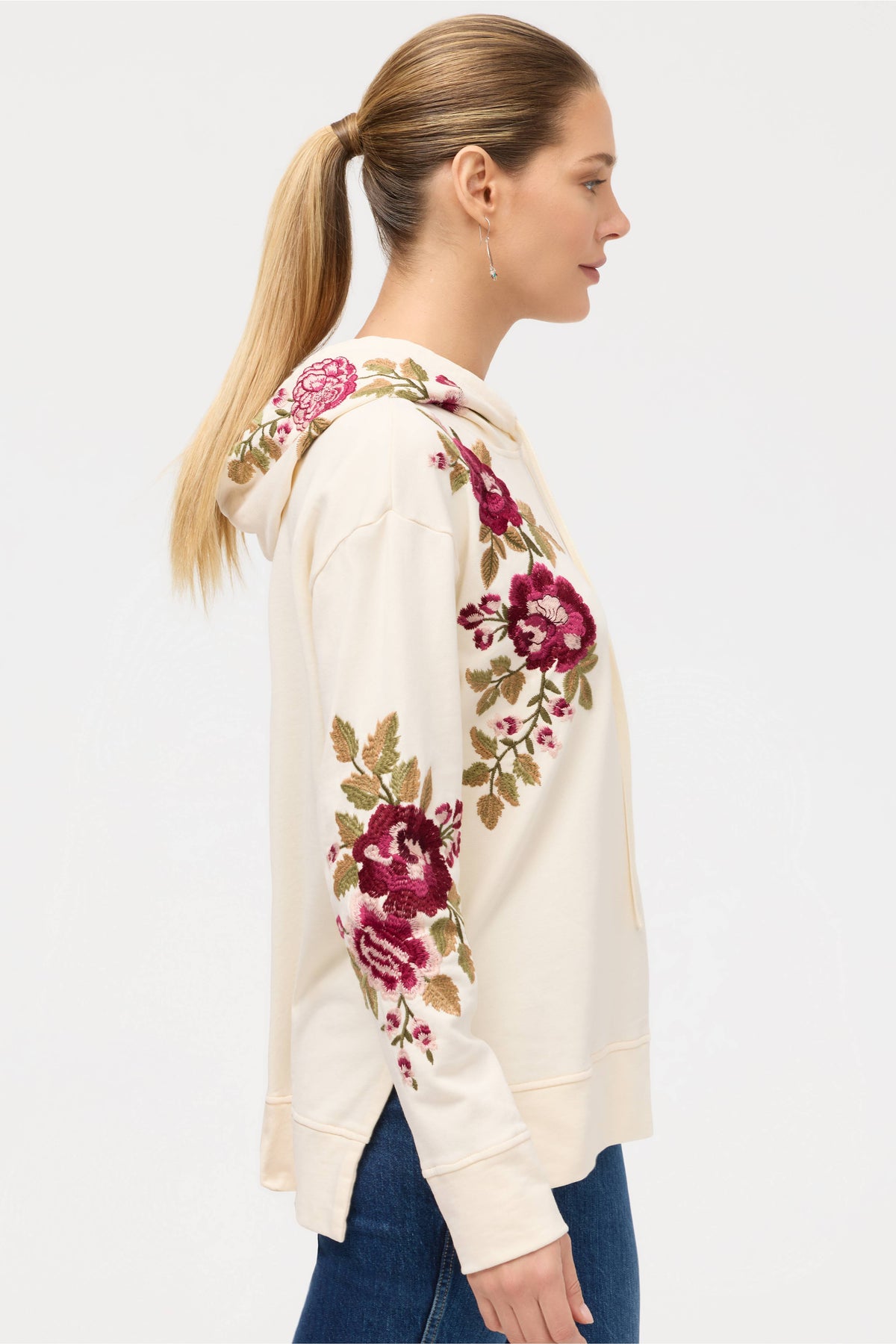 Profile view of a cream hoodie with pink floral embroidery worn by a woman with a ponytail