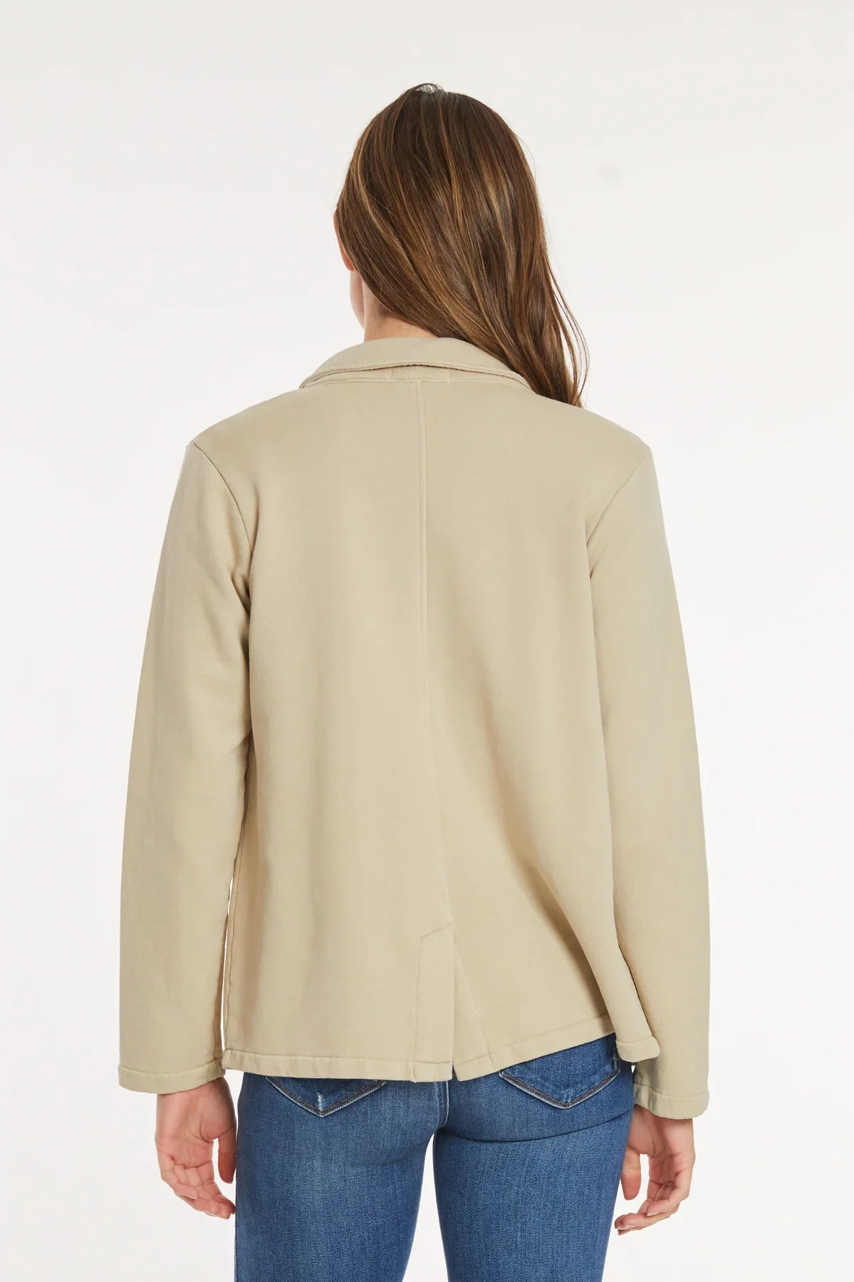 Woman shown from back wearing beige knit blazer with casual blue jeans