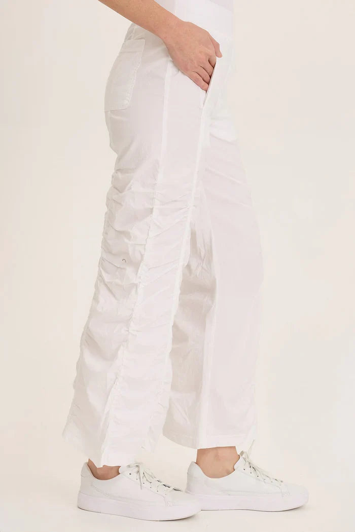 Side angle highlighting the ruched seams and flowy fit of white pants