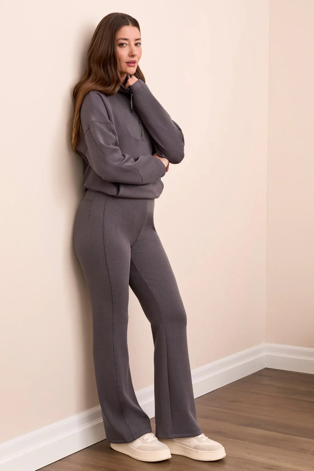 Side view of woman leaning against a wall in a fashionable slate grey ribbed tracksuit