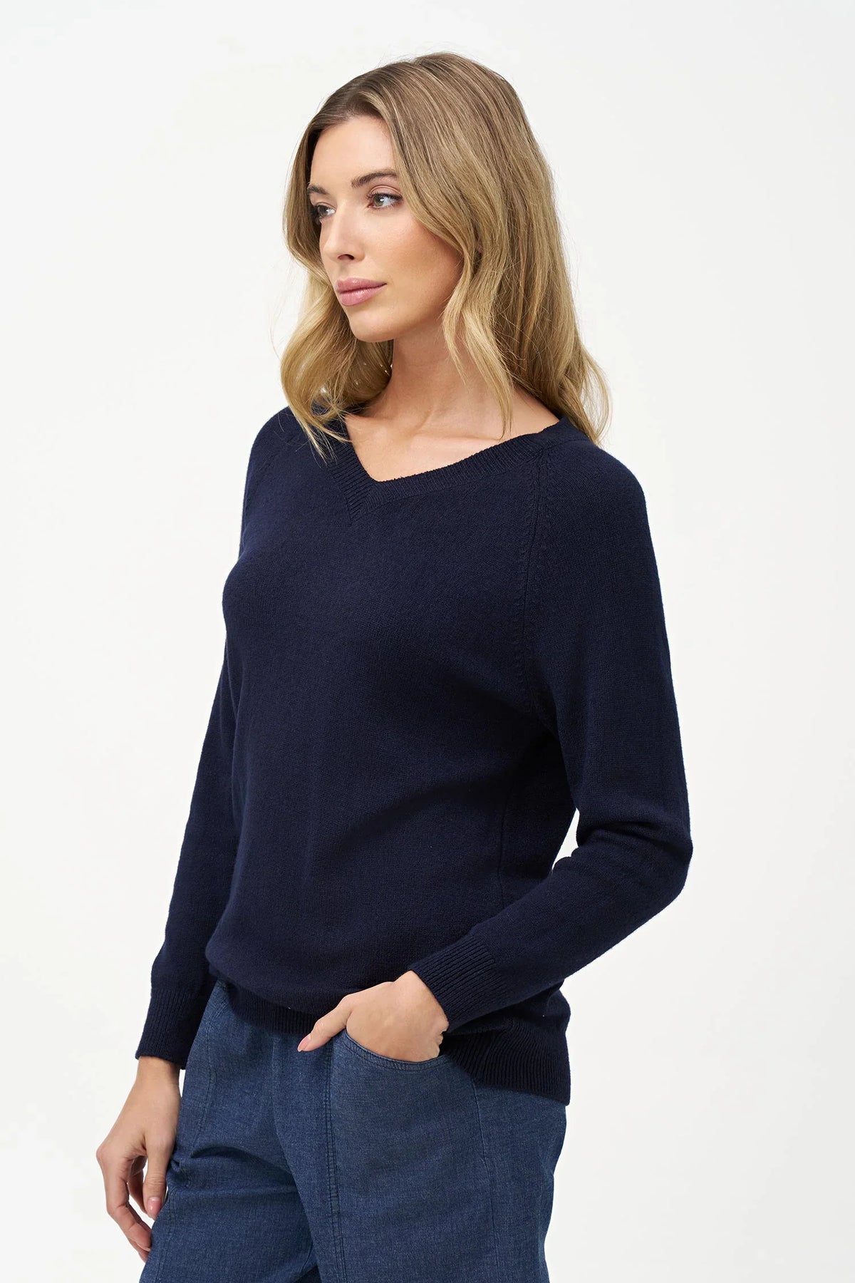 Side view of woman in navy V-neck sweater with hand in pocket