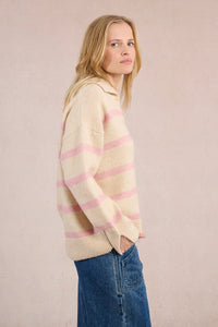 Side profile of a woman modeling a cream and pink striped sweater with relaxed sleeves