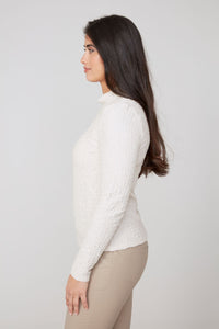 Side profile of woman in fitted ivory textured top paired with beige pants