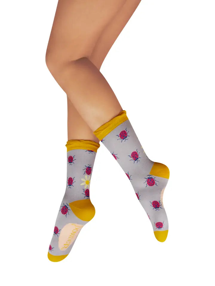 Pair of legs wearing gray crew socks with red ladybug and yellow flower designs