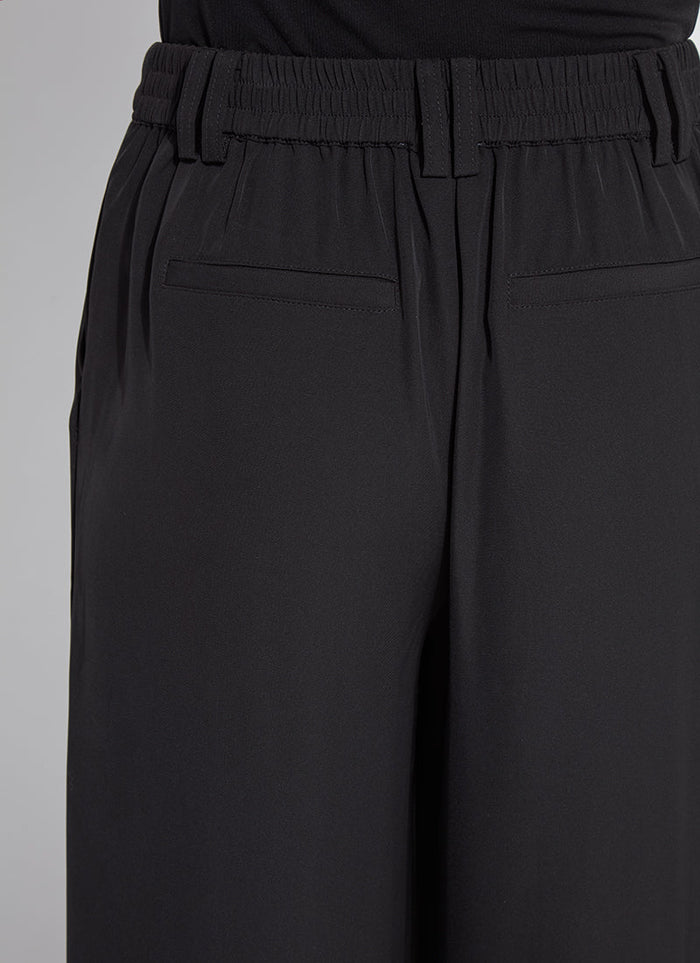 Close up of tailored black wide leg trousers with elastic waistband and slit pockets