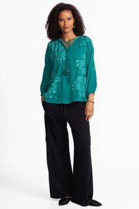 Woman wearing teal long sleeve blouse with floral embroidery and tassel tie front