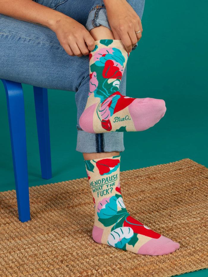 Person wearing colorful Menopause WTF floral socks while sitting on a blue chair
