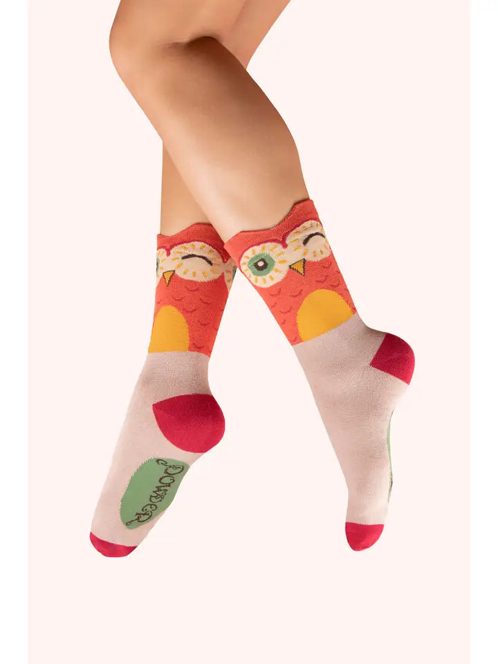 Colorful owl-themed crew socks on crossed legs, featuring playful yellow and red patterns