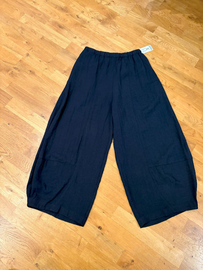 Pair of wide-leg black cotton pants laid flat on a wooden floor