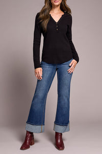 Model standing with one hand on hip, showcasing cuffed wide-leg jeans, black knit top, and red boots