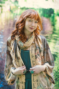 Woman smiling by water wearing scarf with forest deer and whimsical motifs