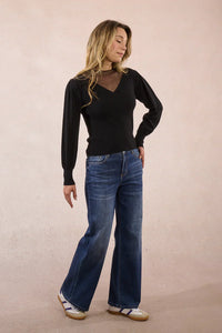 Full body view of woman wearing black mesh detail sweater and blue jeans