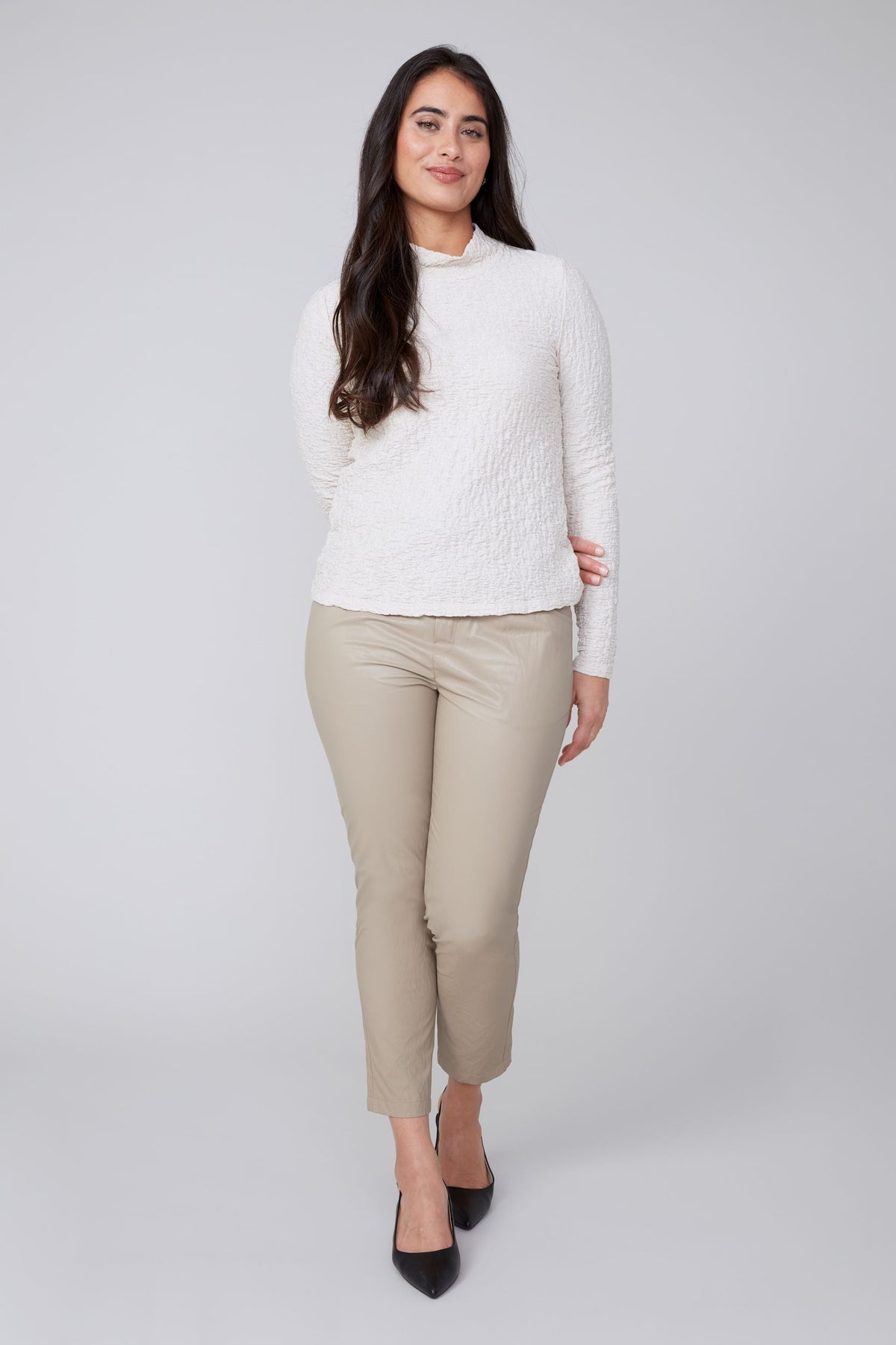Front view of woman wearing textured ivory mock neck top and beige pants
