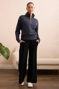 Front view of woman in wide-leg black pants and navy pullover, hands in pockets, standing indoors