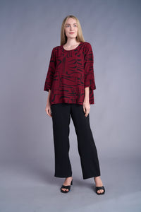 Full-body view of woman in burgundy tunic with black print, paired with black pants and sandals