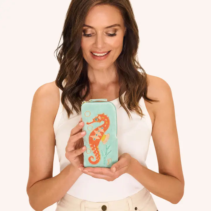 Smiling woman holding turquoise pouch with seahorse embroidery
