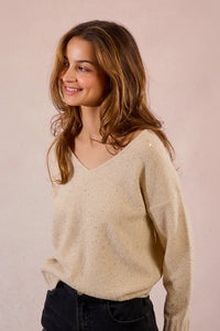 Woman smiling in a champagne V-neck sequin sweater paired with dark jeans