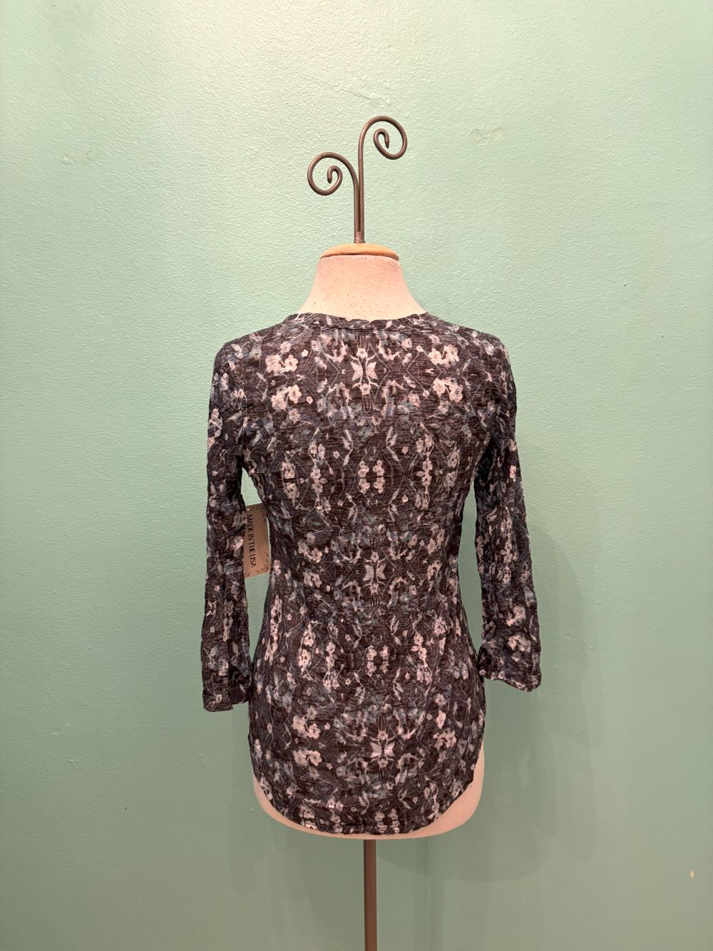 Back view of a women's floral mosaic V-neck top with 3/4 sleeves on a mannequin