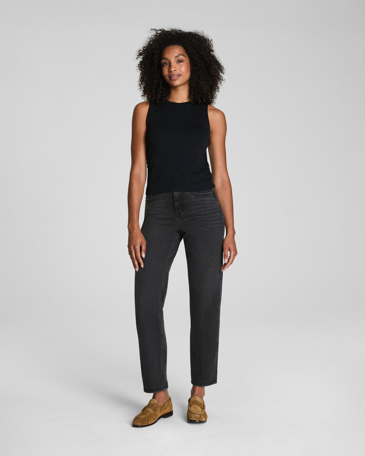 Woman modeling a black sleeveless ruched tank top with dark jeans