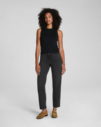 Woman modeling a black sleeveless ruched tank top with dark jeans