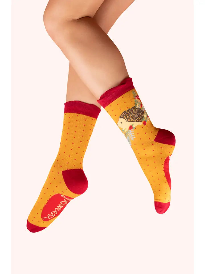 Person wearing yellow polka dot socks with red accents and a cute hedgehog design